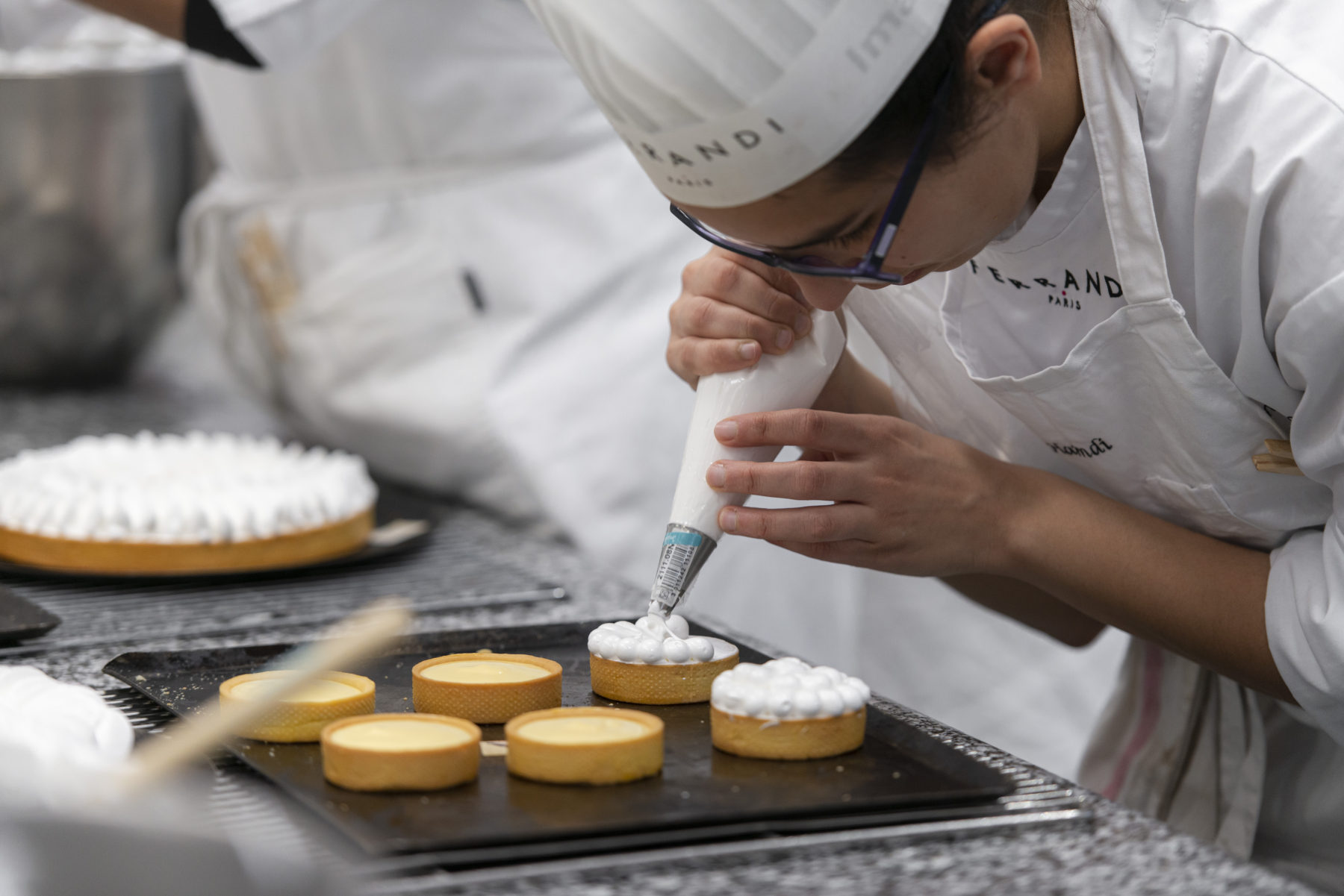 Pastry students piping meringue on tarts